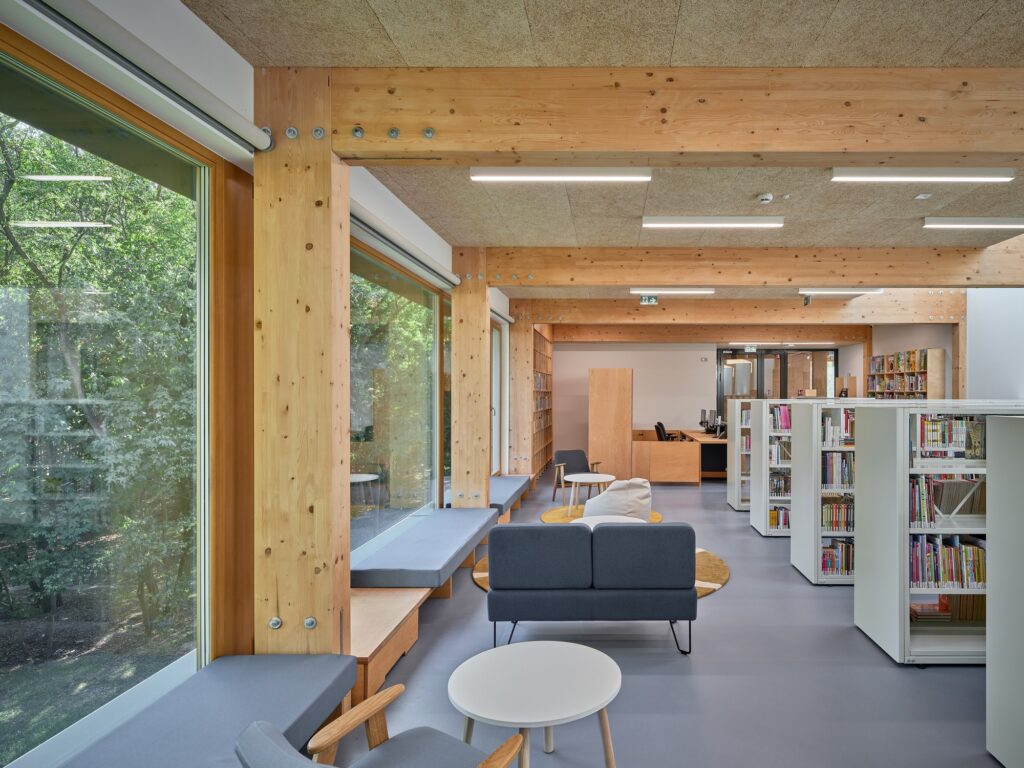 Glulam structural post and beam frame in the main reading room featuring bookshelf aisles and soft seating areas.