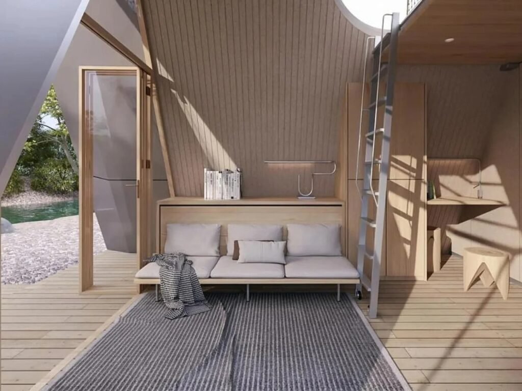 Bright living room area inside Camping House with daytime couch configuration, desk, ladder, and glass doors opening to outdoor views.