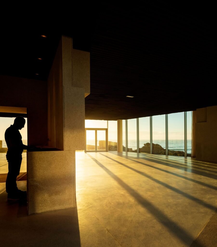 Interior shadow view of a silhouette near a reception counter inside Cresmina Fort with sunlight streaming through large glass facades.