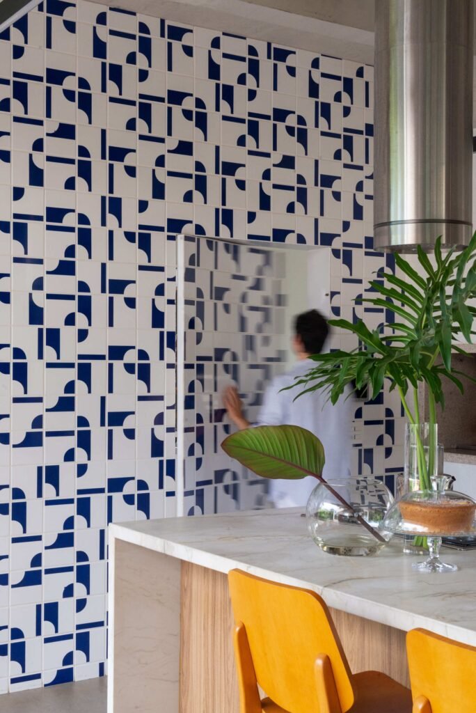 Kitchen counter with orange stools in front of a blue and white geometric patterned tile wall with a hidden door.