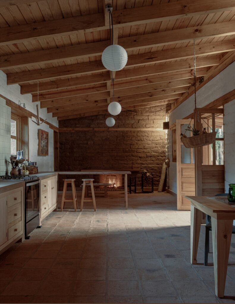 Wide internal view of the open living room at Casa Esteli highlighting the fireplace embedded in the original adobe wall, timber ceiling, and paper pendant lights.