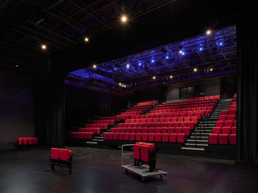 Flexible black box theater interior at Le Grand-Espace featuring retractable red seating tiers and blue overhead technical lighting.