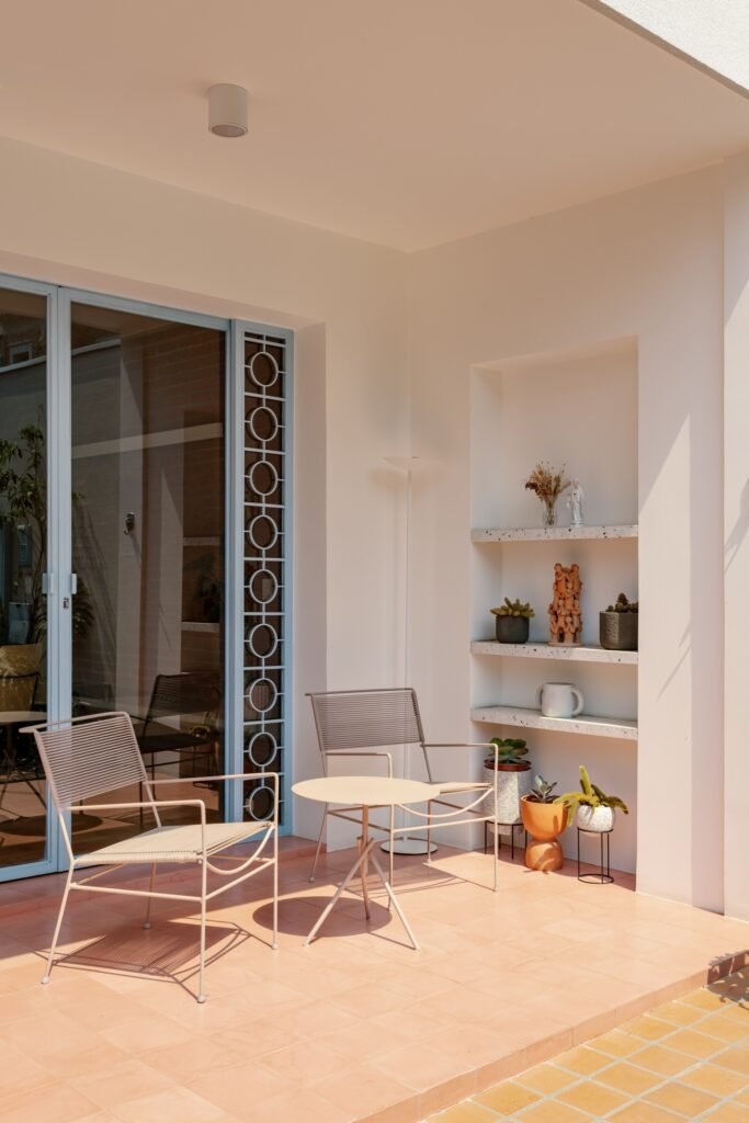 Outdoor patio area with terracotta floor tiles, modern light grey chairs, and recessed wall shelves.