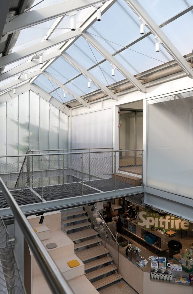 View looking down into the bistro coffee counter from an upper walkway under a translucent pitched glass roof at Spitfire Roastery.