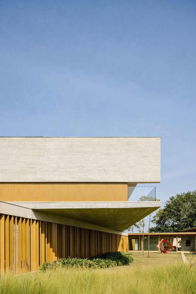 Low-angle shot of a cantilevered concrete upper level over wooden slatted ground-floor walls.
