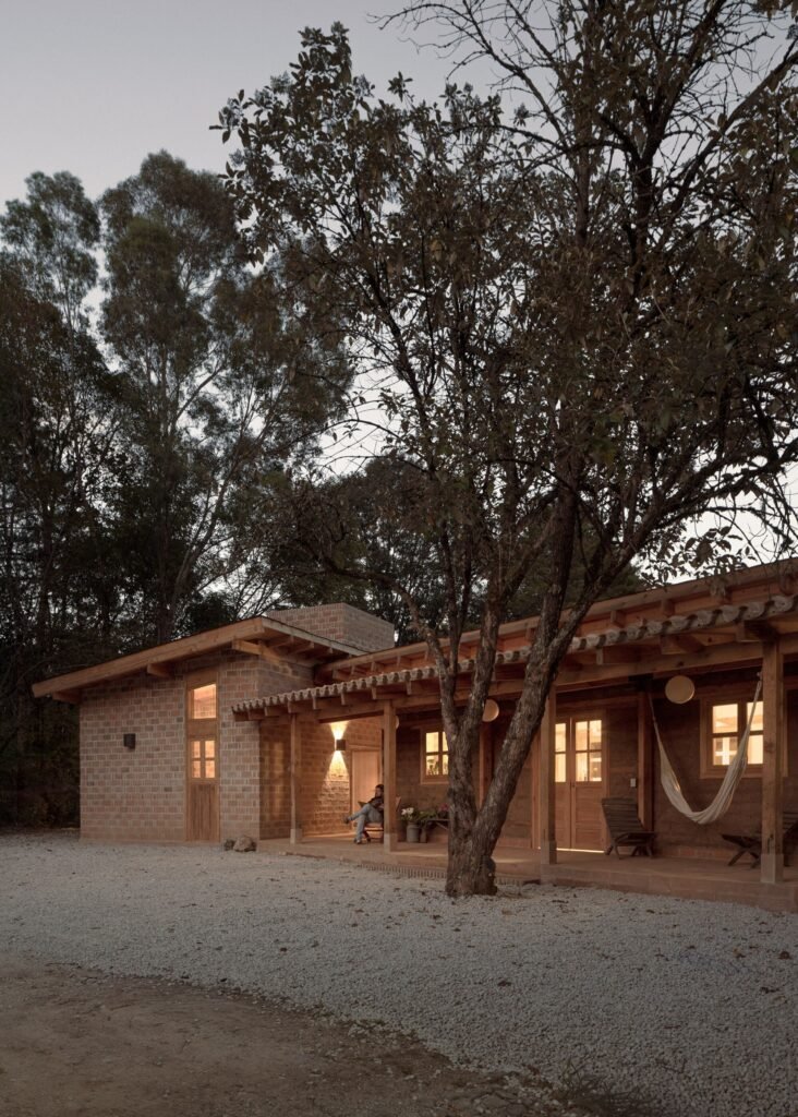 Dusk view of Casa Esteli's exterior elevation showing warm interior lighting glowing through wooden doors and windows along the veranda.