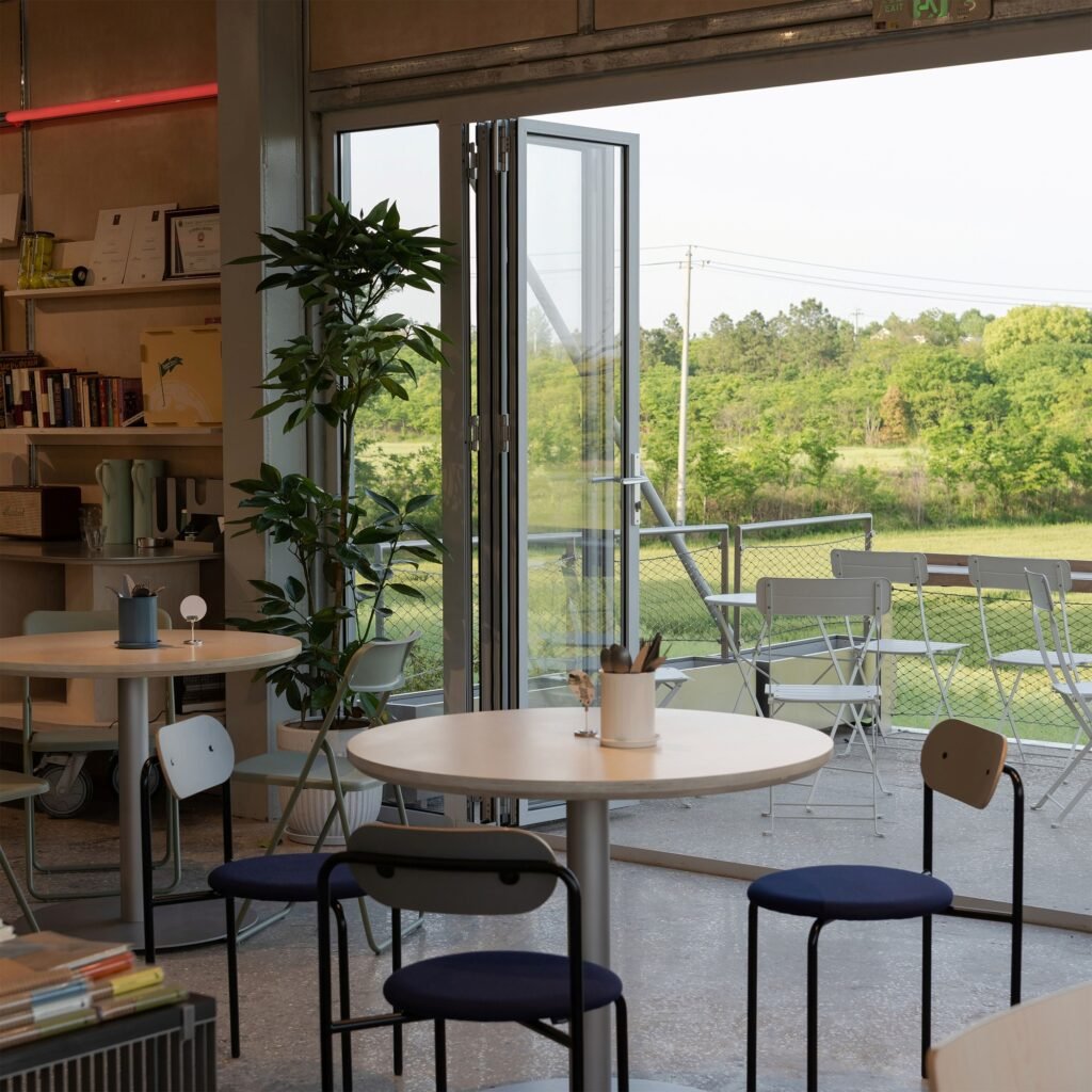 Indoor dining tables and chairs facing open bifold glass doors leading out to a terrace overlooking green fields.