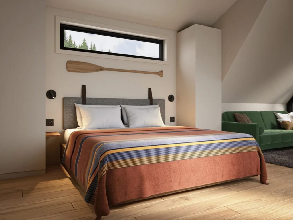 Master bedroom area in the A-Frame Bunkhouse with a queen-sized bed, striped blanket, decorative wooden oar on the wall, horizontal window, and built-in closet storage.