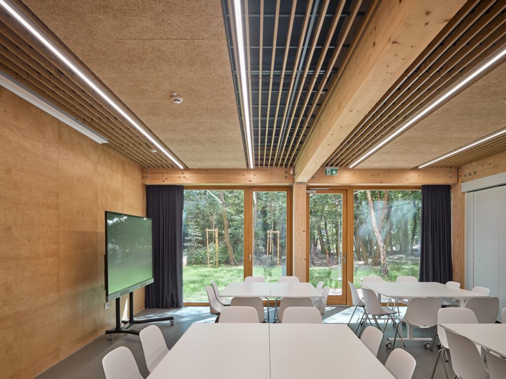 Multifunctional conference room with reconfigurable white tables, interactive digital display, and large garden-facing windows.