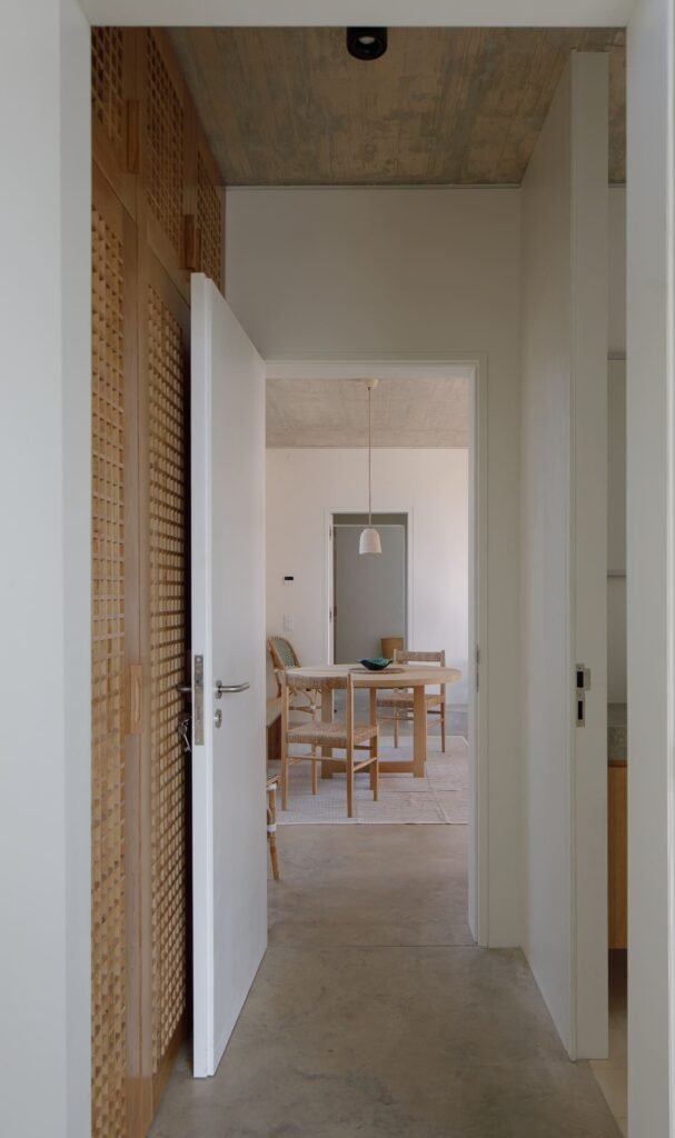 Interior corridor in Melides MG House featuring latticed wooden cabinet doors leading to a light-filled room.