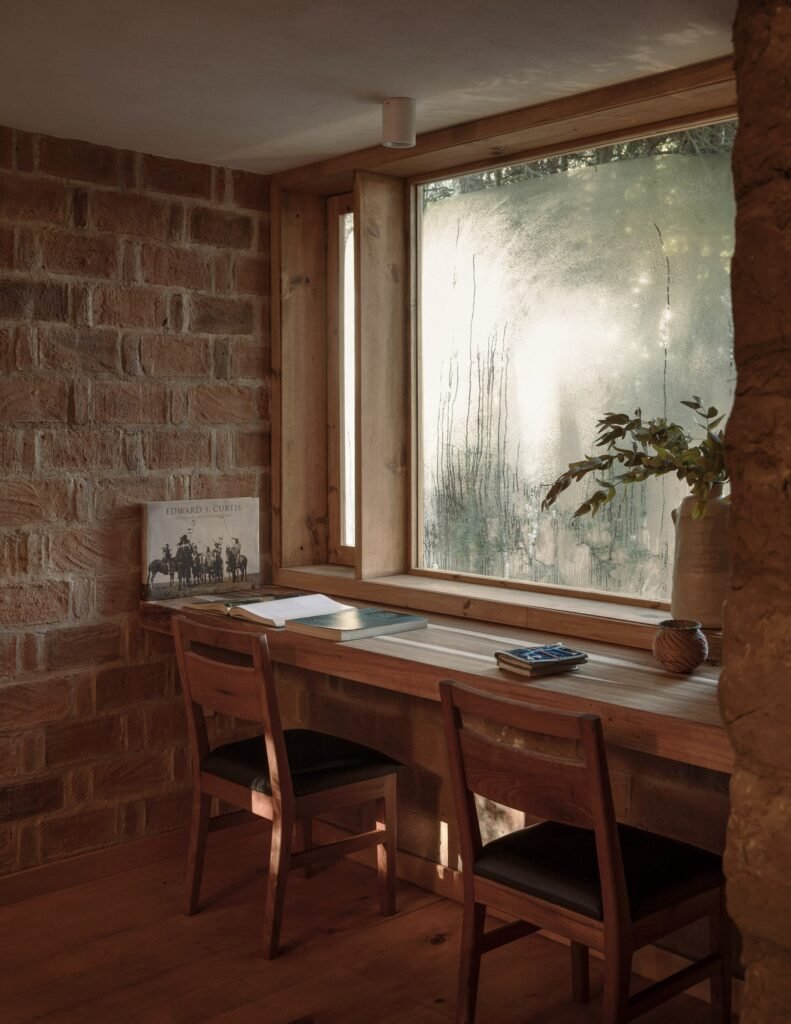 Interior study bench built into a deep window opening with frosted glass, positioned between exposed red brick and adobe walls.