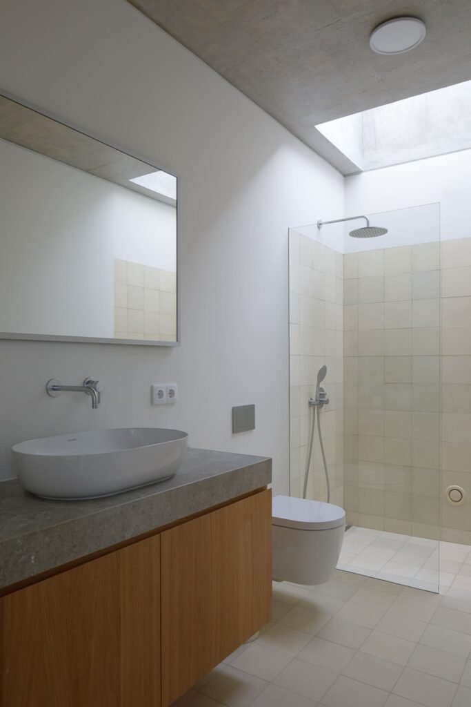 Modern bathroom in Melides MG House featuring stone countertop, oval vessel sink, wooden vanity, and glass shower enclosure.