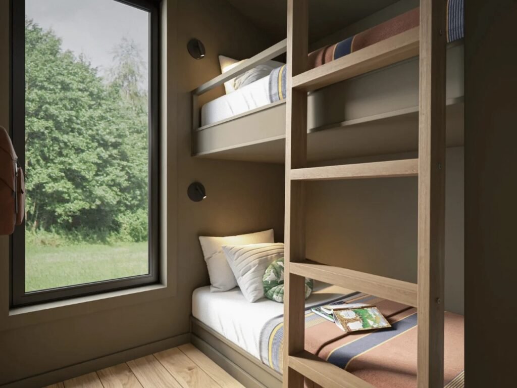 Close-up of custom built-in wooden bunk beds with integrated reading lights, storage shelf, and a tall vertical window letting in natural light from the forest outside.