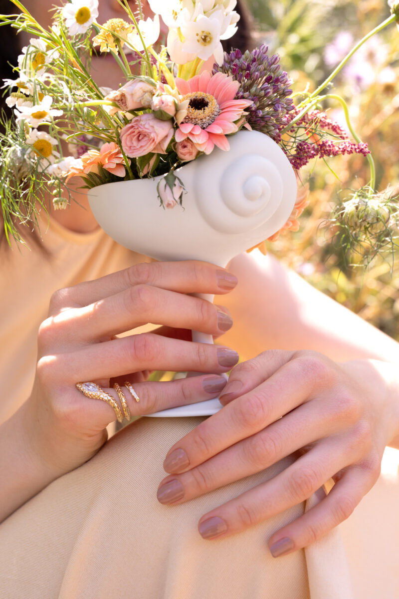 A hand holds a white shell-shaped vase filled with flowers from the L’OBJET x Jessica McCormack collection.