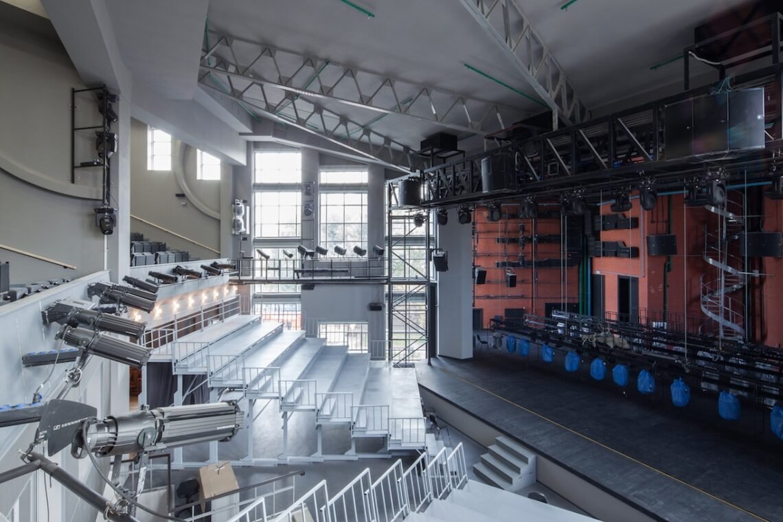 Auditorium interior showing tiered seating, stage space and large windows