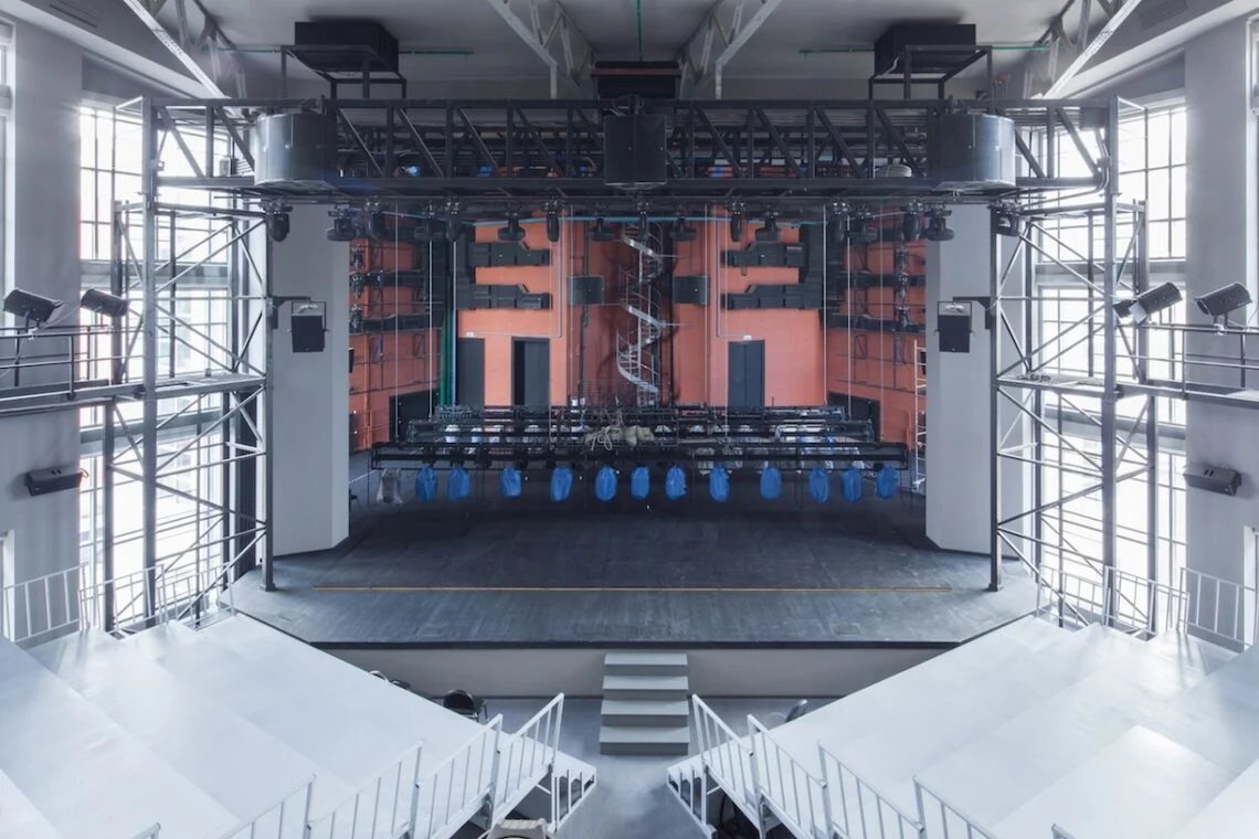 Auditorium interior showing tiered seating, stage space and large windows