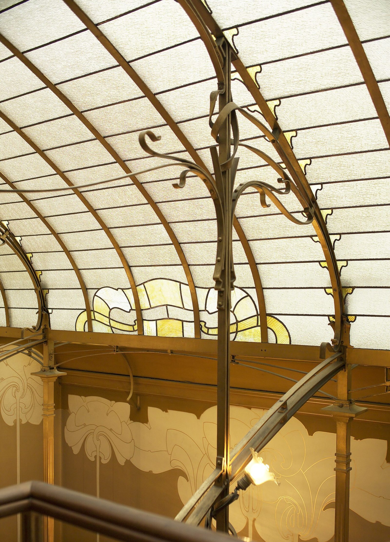 Curved glazed roof, slender metal framing and painted wall decoration above the staircase in Victor Horta's house in Brussels.