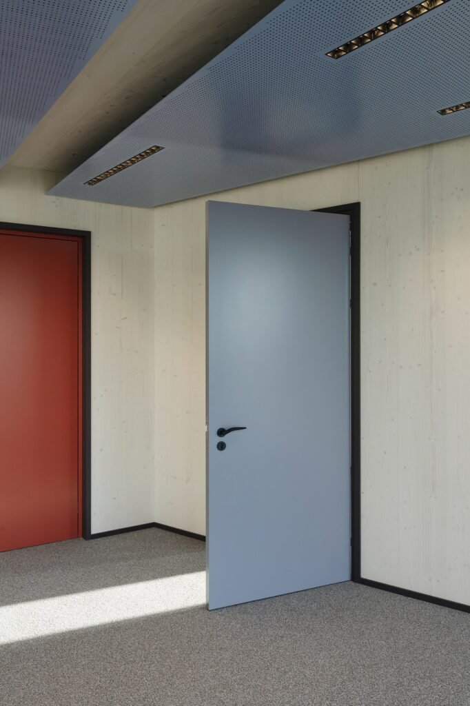 Exposed timber, coloured doors and suspended ceiling panels in an office interior.