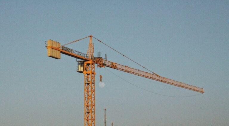 Yellow construction crane against a blue sky. | رافعة بناء صفراء أمام سماء زرقاء.