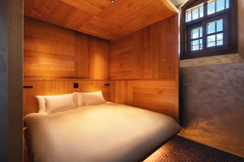 Bedroom with a timber-lined sleeping area beside an exposed brick wall and high window