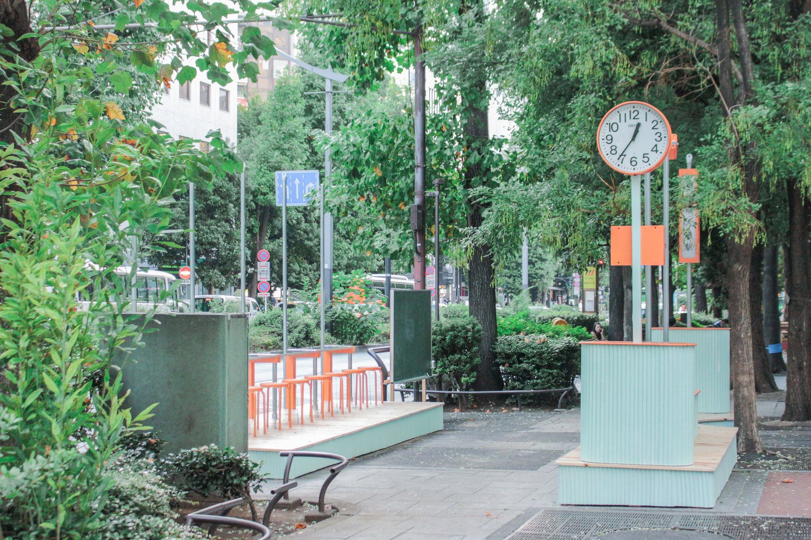 Two pale-green platforms, orange stools and a clock on Green Boulevard.