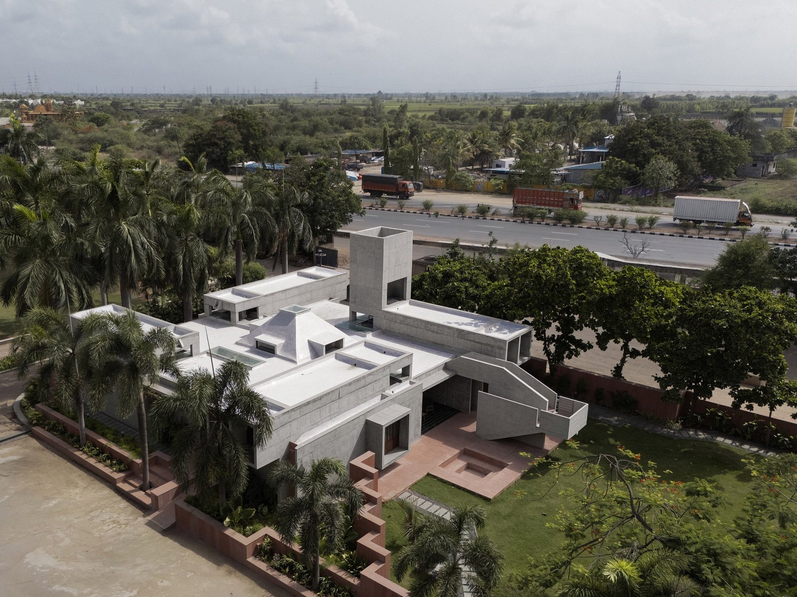 Aerial view of Monastic Field’s clustered concrete volumes beside the temple precinct in Baleshwar