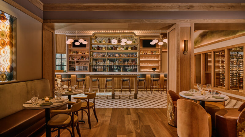 A wide timber-framed opening connects dining tables to the bar across a change in flooring.