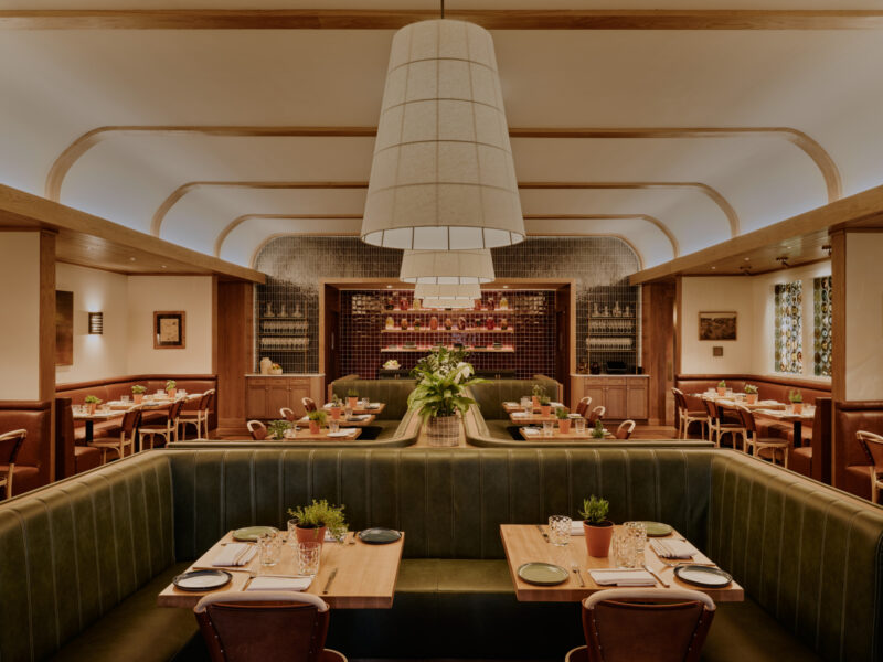 Olive booth backs divide the main dining room beneath a pale curved ceiling and a line of large pendants.