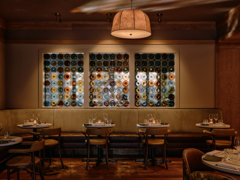 Colored glass rondels sit directly above the banquette, with brighter glazing and a darker ceiling.