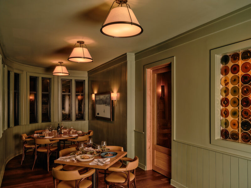 Green wall panels, a glazed door and smaller pendants give the side room a more enclosed scale.