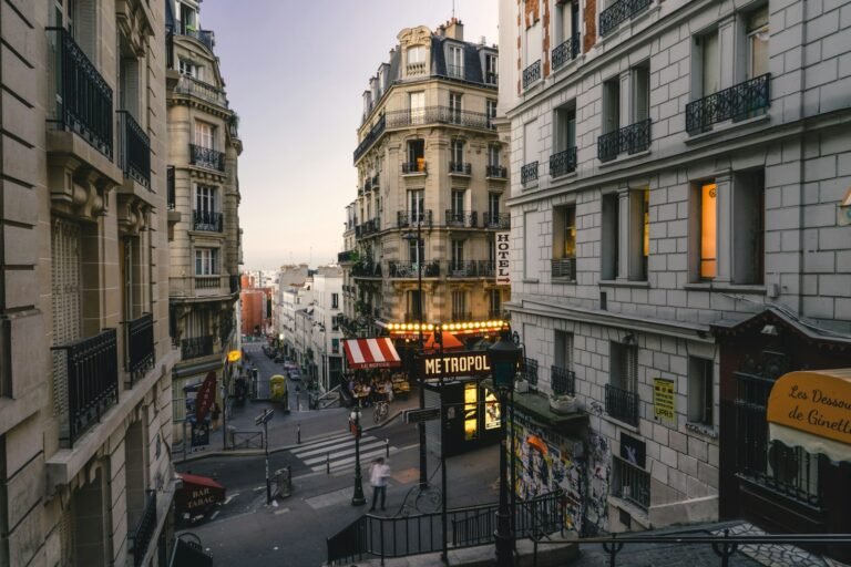 Paris street at dusk with continuous building frontages, pavements and pedestrians.