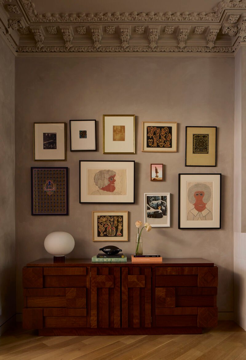 A group of artworks sits between the sideboard and the surviving cornice.