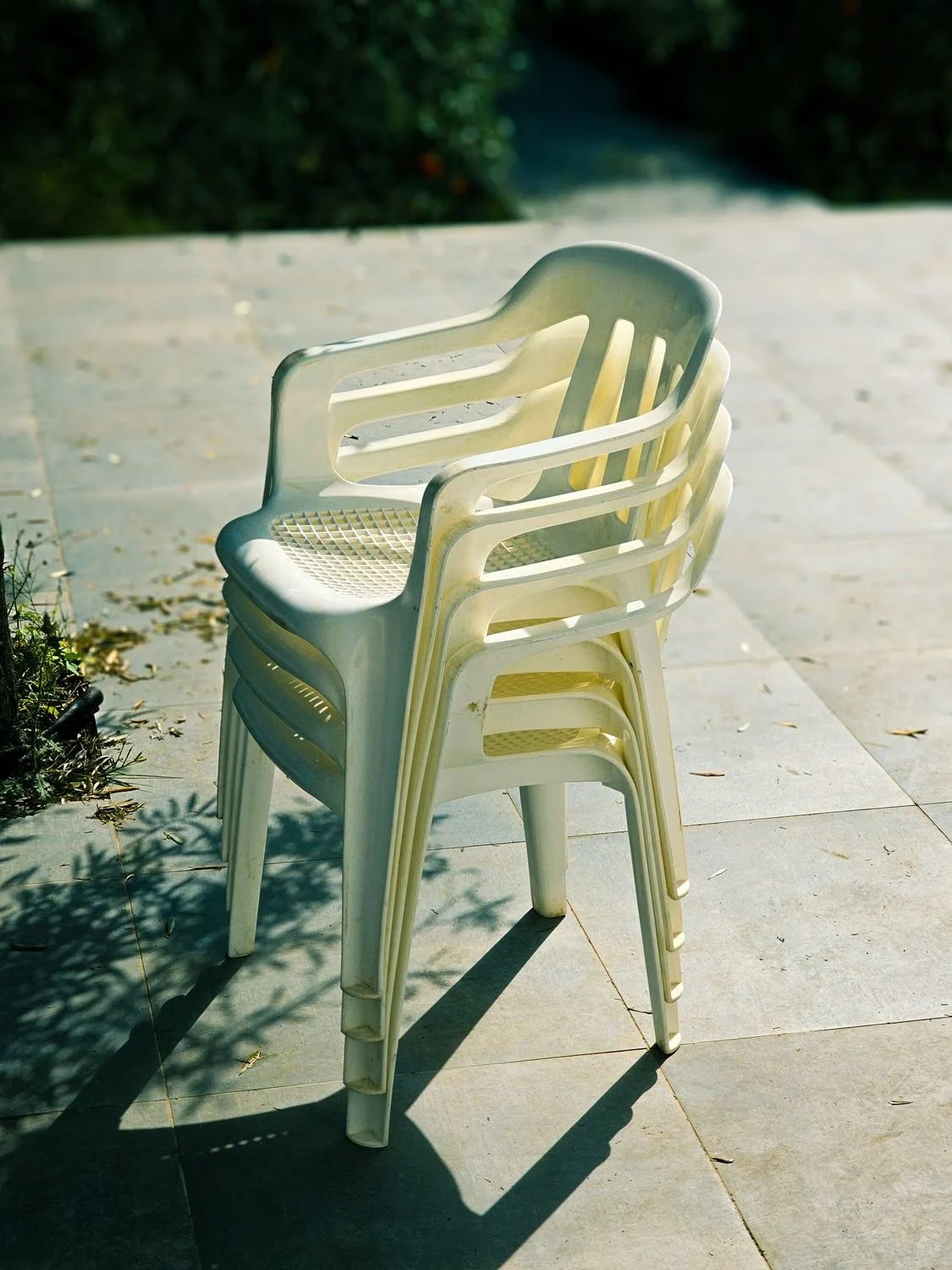 Four white monobloc plastic chairs nested in a stack on a sunlit patio