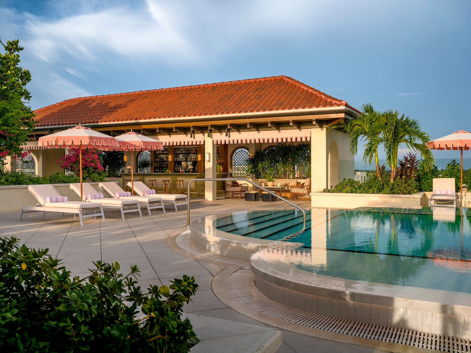 Rooftop pool at the Nora Hotel beside a tiled-roof pavilion and pink fabric umbrellas
