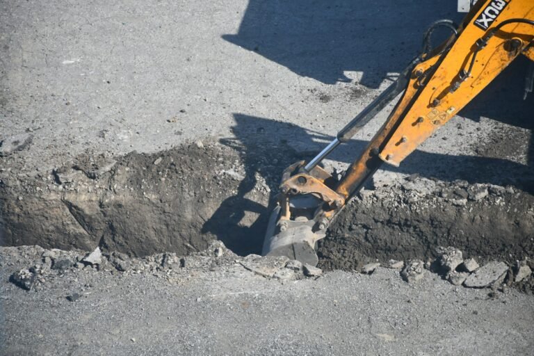 Excavator digging a trench in a road; illustrative infrastructure construction photograph.