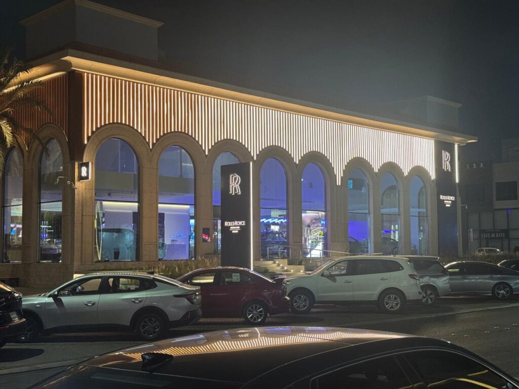 واجهة خارجية لصالة عرض رولز رويس مضاءة ليلاً مع سيارات متوقفة في الخارج