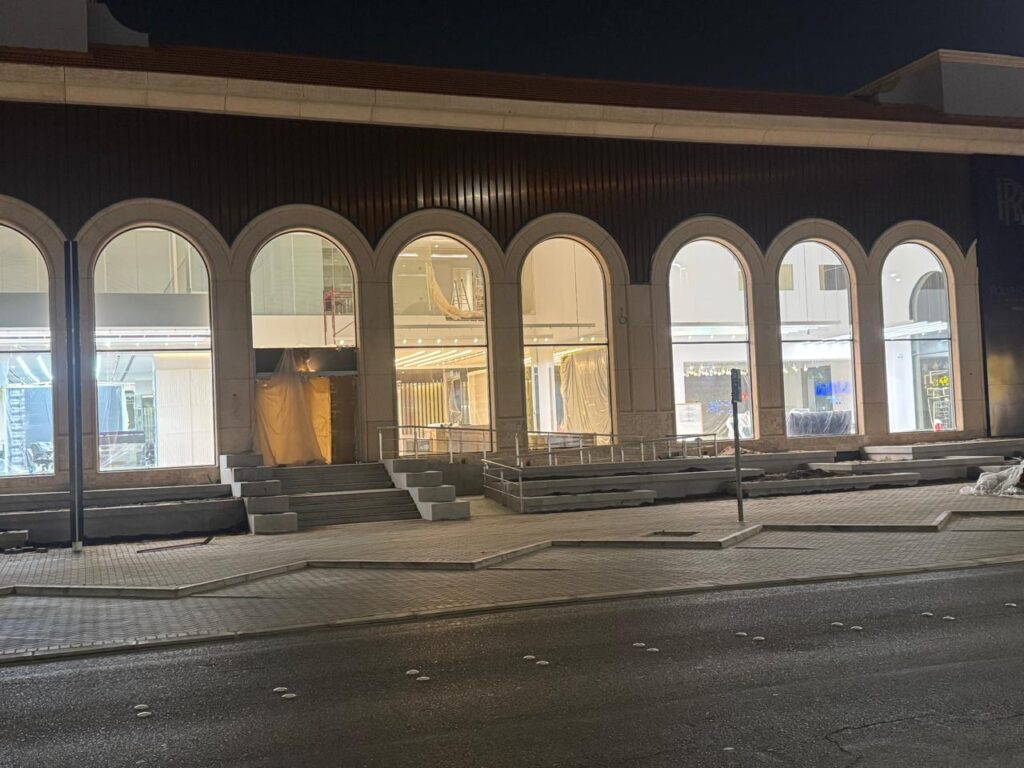 واجهة مبنى حديثة مضاءة ليلاً تتميز بنوافذ مقوسة كبيرة ودرجات المدخل