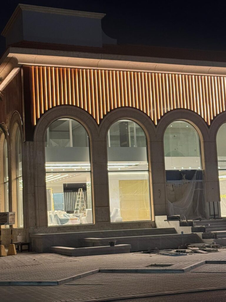 واجهة مبنى حديثة ليلاً مع نوافذ مقوسة مضاءة وشريط إضاءة LED عمودي زخرفي في الأعلى