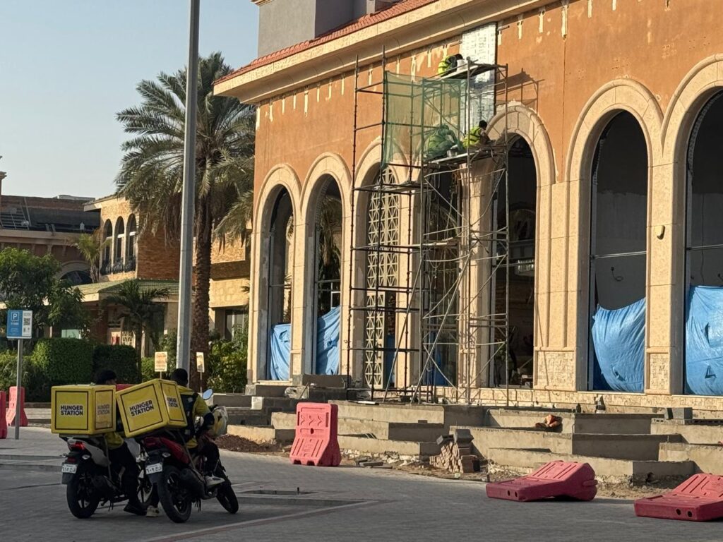 عمال توصيل هنقرستيشن على دراجات نارية أمام مبنى قيد الترميم والسقالات المعدنية