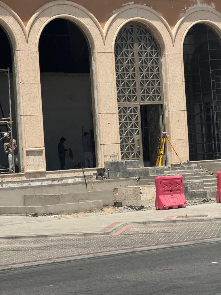 عمال بناء داخل مبنى ذو أقواس كبيرة، مع جهاز مساحة منصوب في الخارج