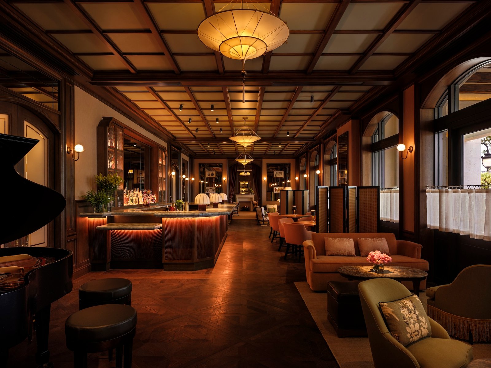 Dark timber ceiling grid above the Nora Hotel bar, with window-side seating and a lit counter