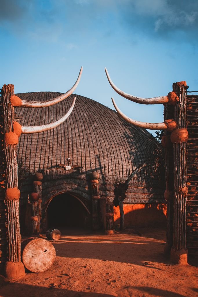 A domed thatched building behind a timber entrance decorated with large curved horns.