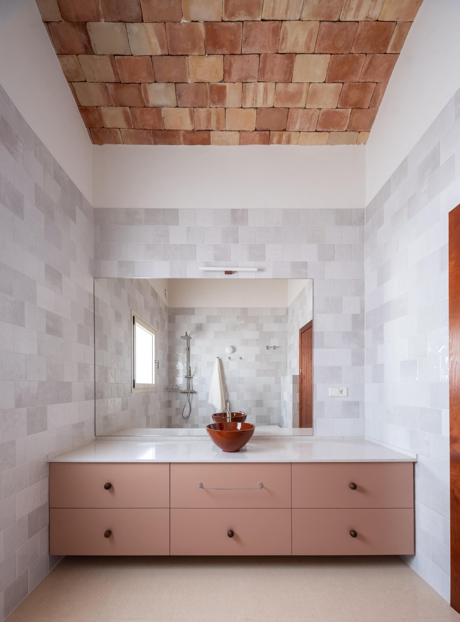 A wide vanity combines pink cabinetry with pale wall tiles.