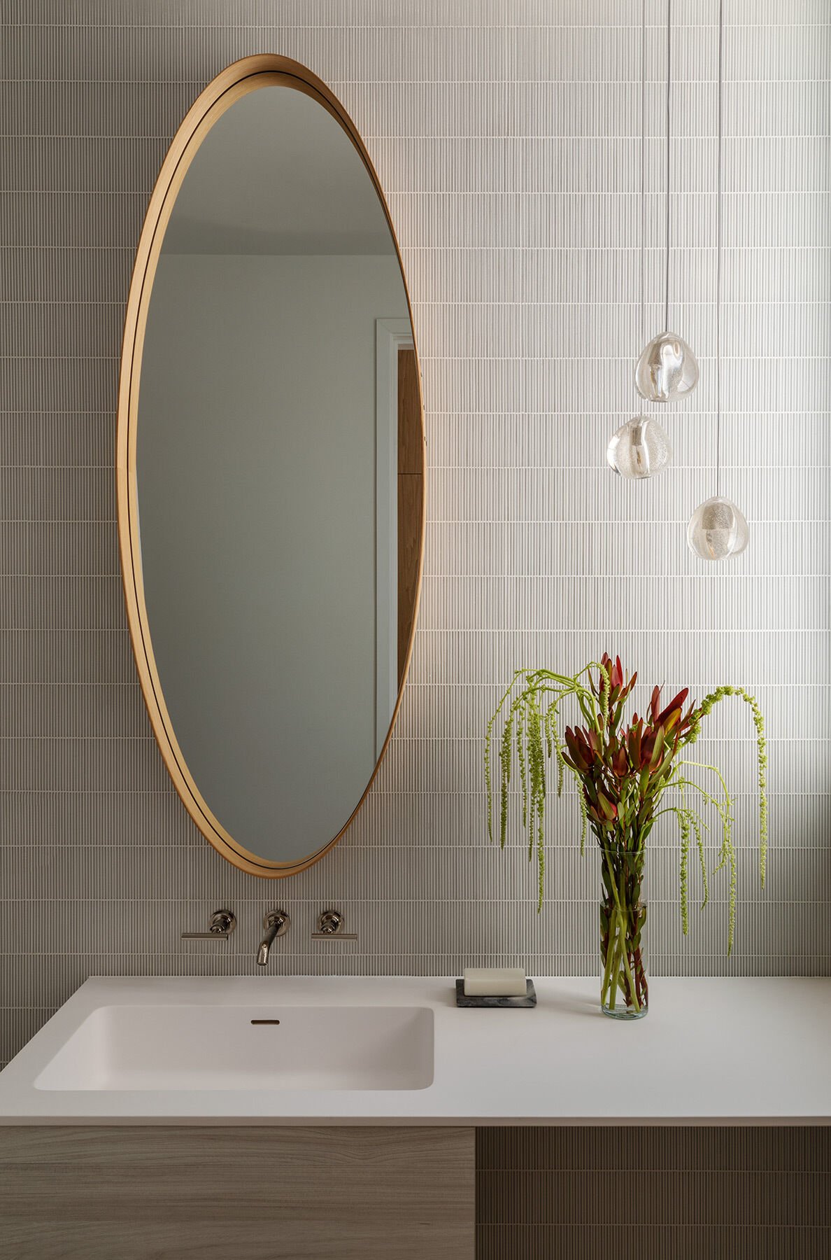 An oval timber-framed mirror softens a wall of fine vertical tiles.