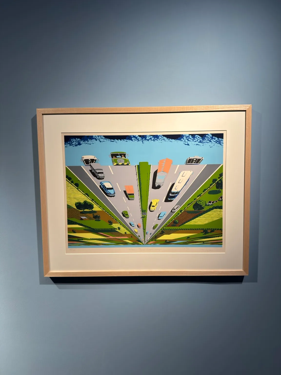 A framed colourful artwork showing a steeply converging urban road scene, vehicles and green spaces at Hayy Jameel.