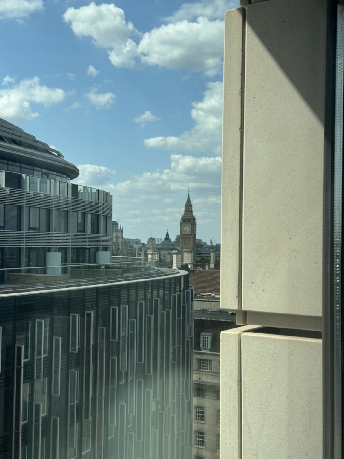 View through a window towards London's clock tower, partly framed and obscured by nearby buildings