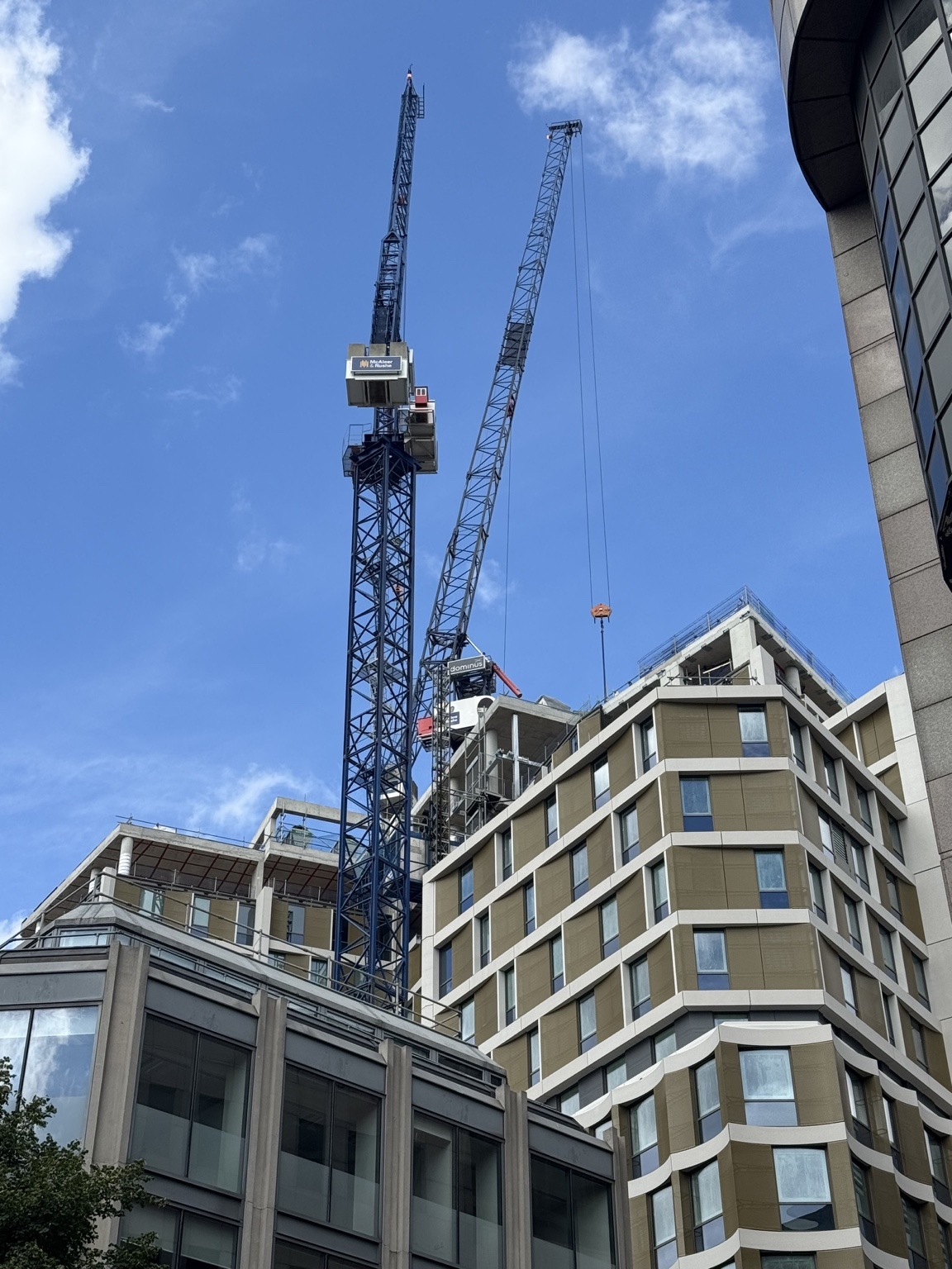 Two cranes above buildings with exposed upper structural elements and adjacent facades