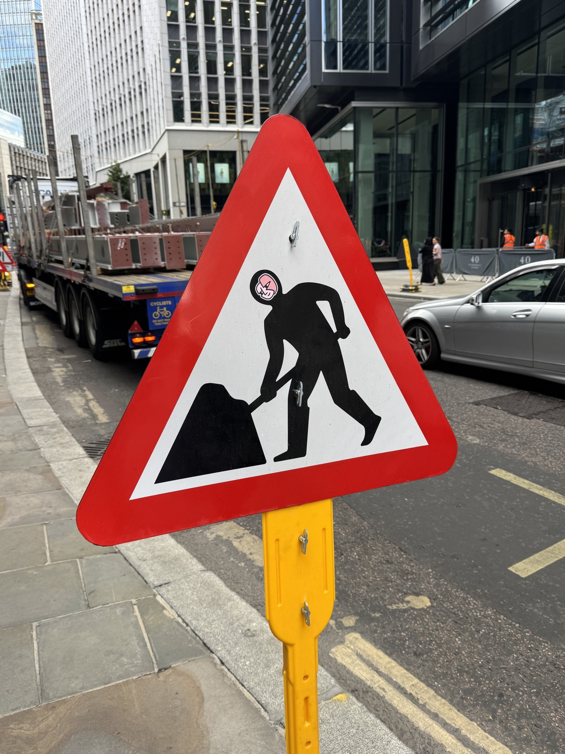 Roadworks warning sign beside a pavement with a truck, car and buildings behind it