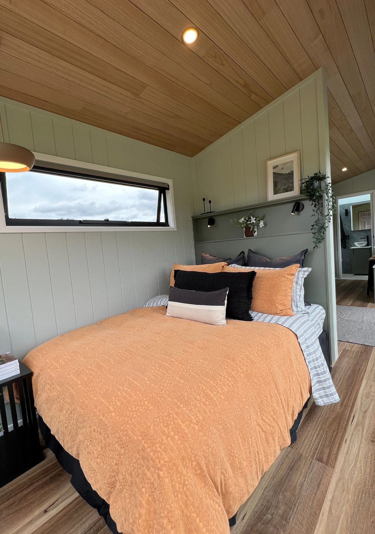 Bedroom with a horizontal window, pale green walls and a timber ceiling