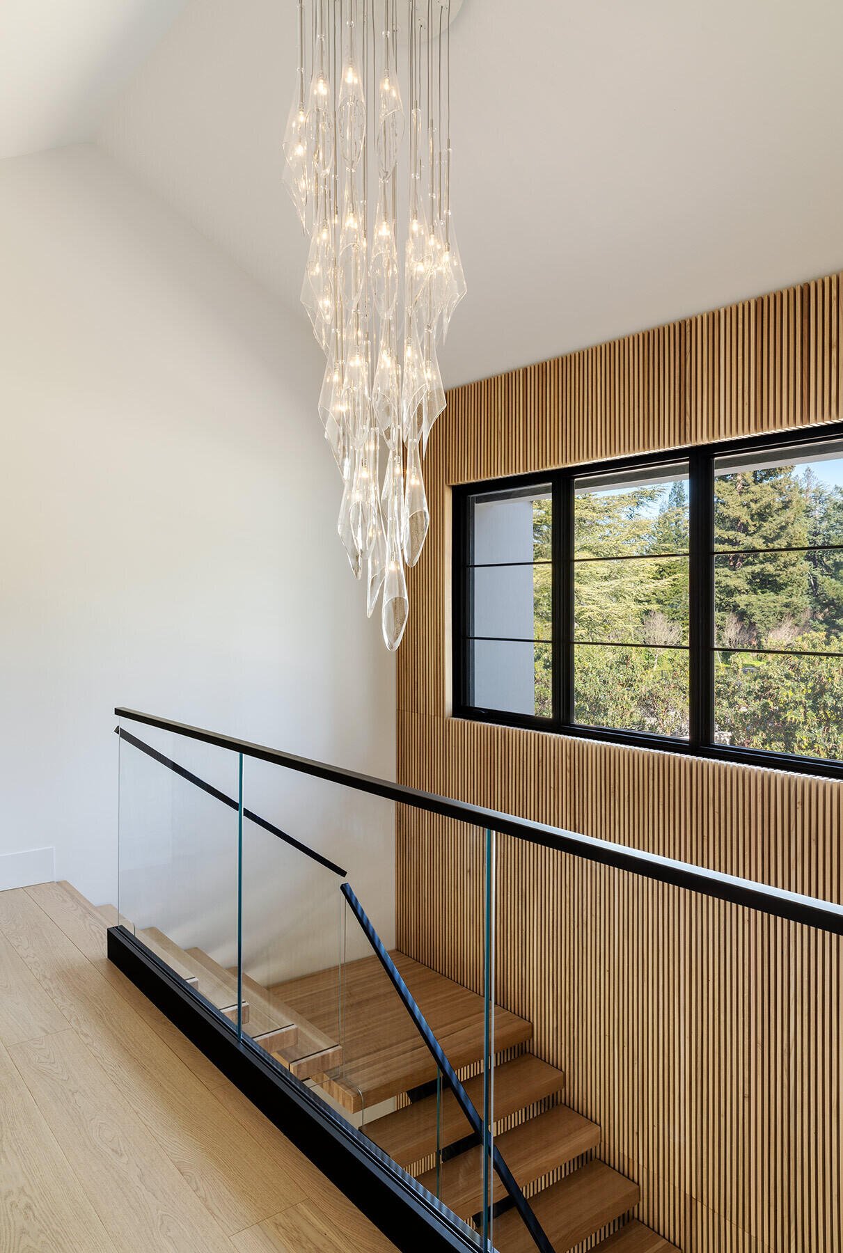 Timber treads, glass balustrades and a slatted wall frame the staircase.